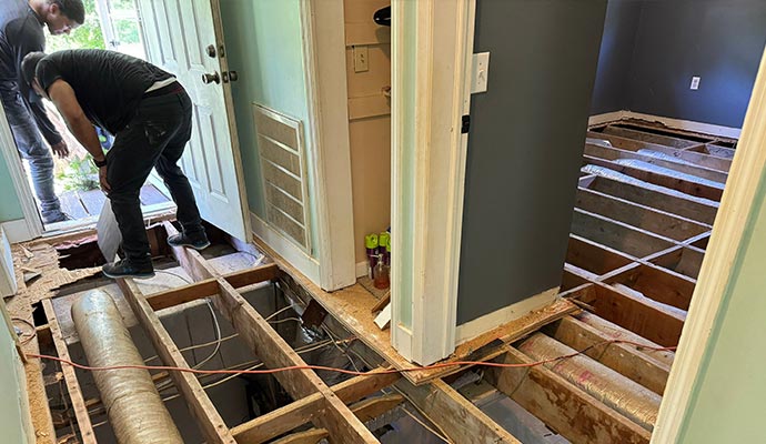 Complete floor and subfloor replacement due to severe damage Workers removing a damaged floor and subfloor, exposing the joists below