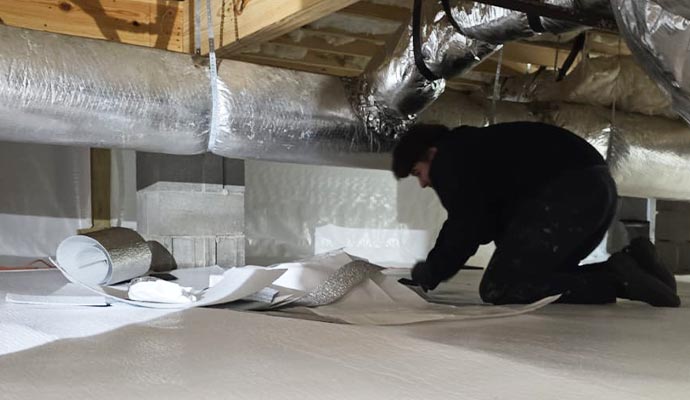 Professional crawlspace encapsulation and vapor barrier installation A worker installing a white vapor barrier during a crawlspace encapsulation