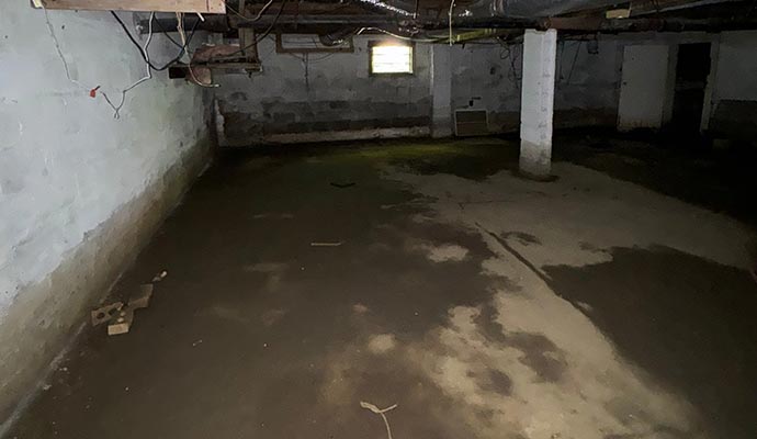 Basement with damp concrete floor and visible water stains along the walls