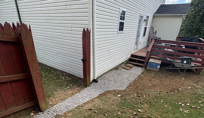 A newly installed exterior French drain with gravel along a house foundation A newly installed exterior French drain with gravel along a house foundation