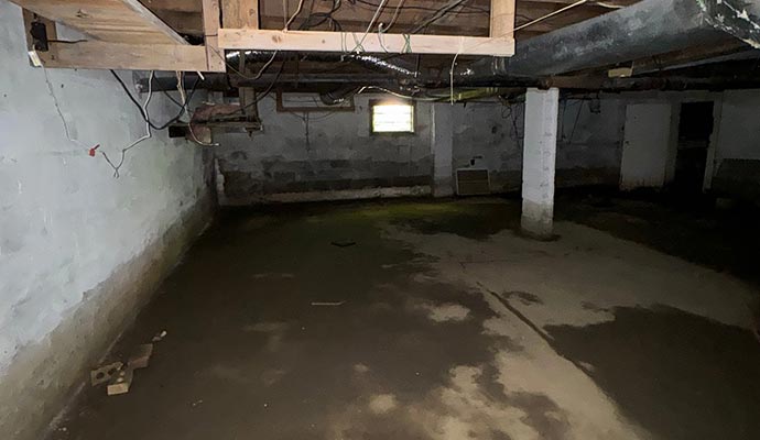 A dark, flooded basement with standing water on a concrete floor and exposed ceiling joists