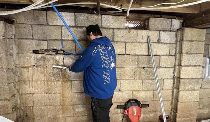 A technician working on a concrete block foundation wall with visible horizontal cracks and water staining
