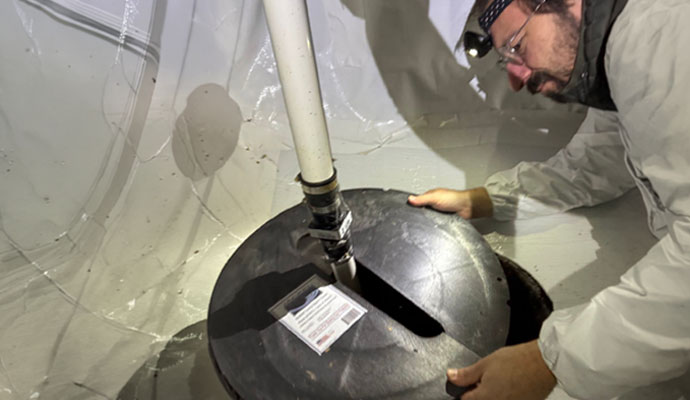 Technician repairing a sump pump pit in a crawl space