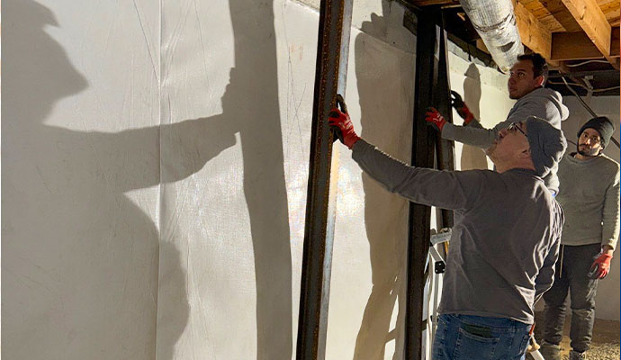 Technicians installing steel I-beams to reinforce a basement foundation wall